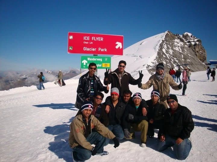 Friends in the snow at Glacier Park, by the Ice Flyer chairlift sign, in the Swiss Alps